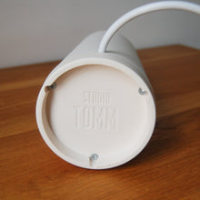 Load image into Gallery viewer, bottom of white lamp base showing studio tomm logo and screws that secure the two parts together