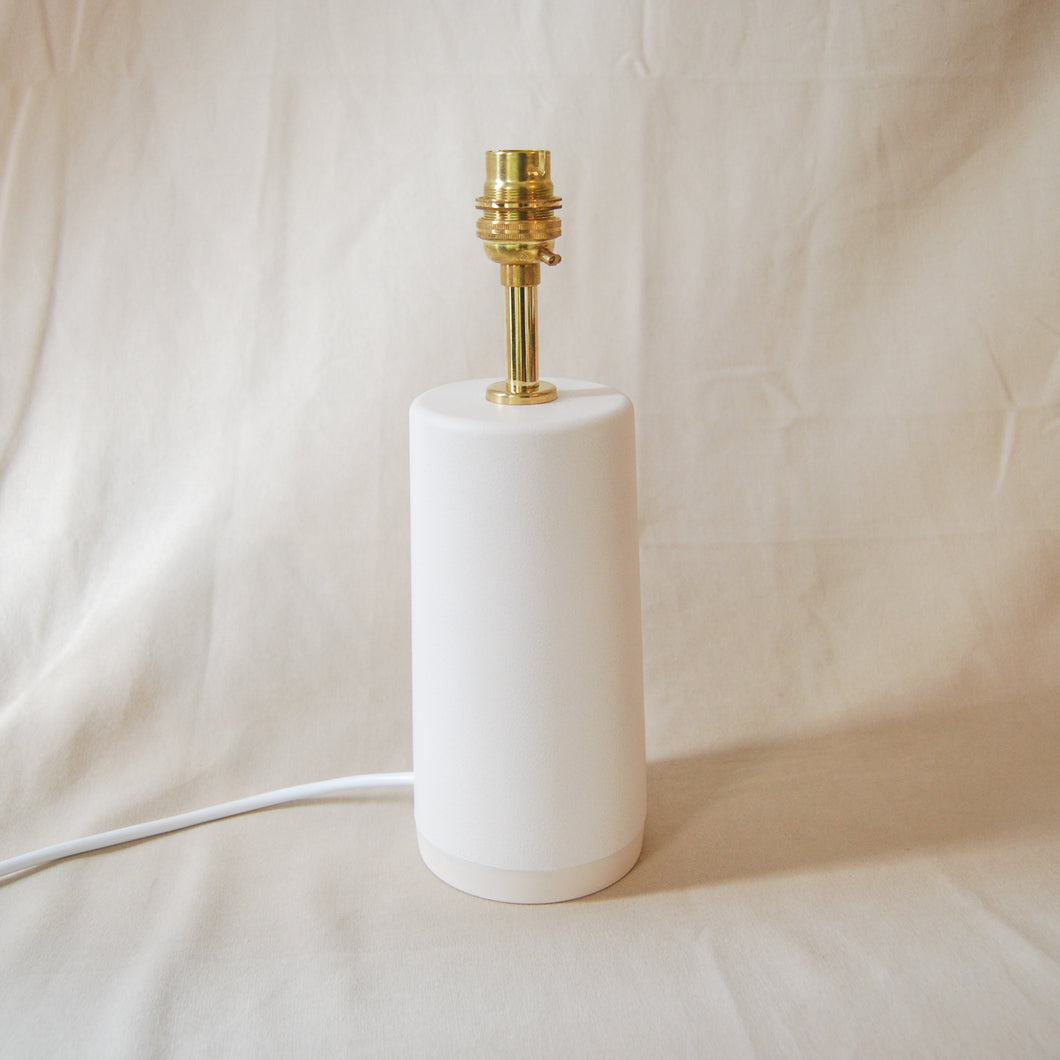 white lamp base with brass fitting and white power cord on a neutral background